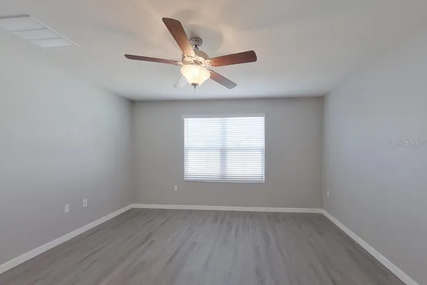 an empty room with wooden floor fan and windows