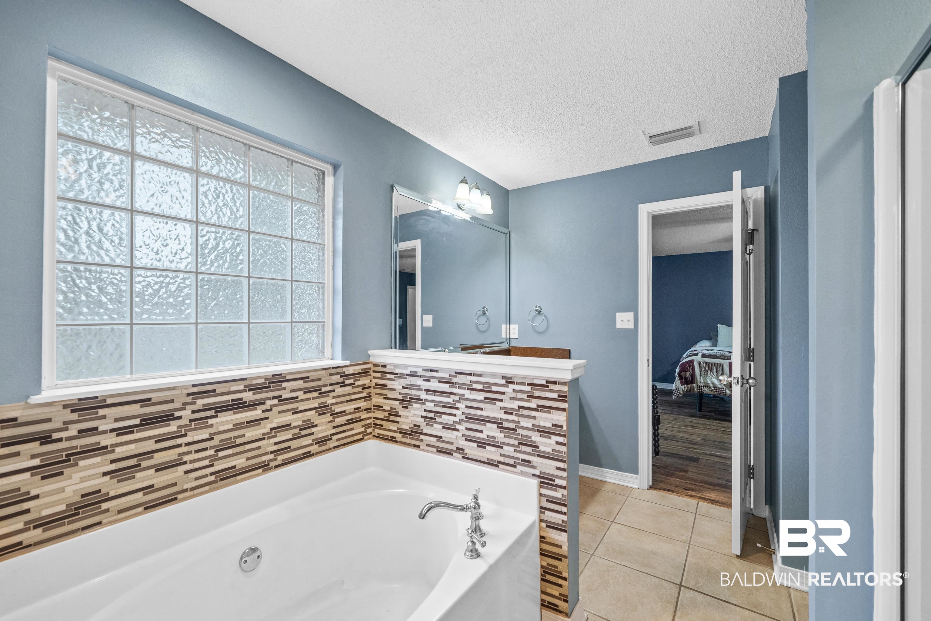 9552 Collier Loop Daphne, AL 36526 - Photo 19 of 28 Ensuite bathroom featuring a bath, tile patterned flooring, a textured ceiling, two vanity areas, and baseboards