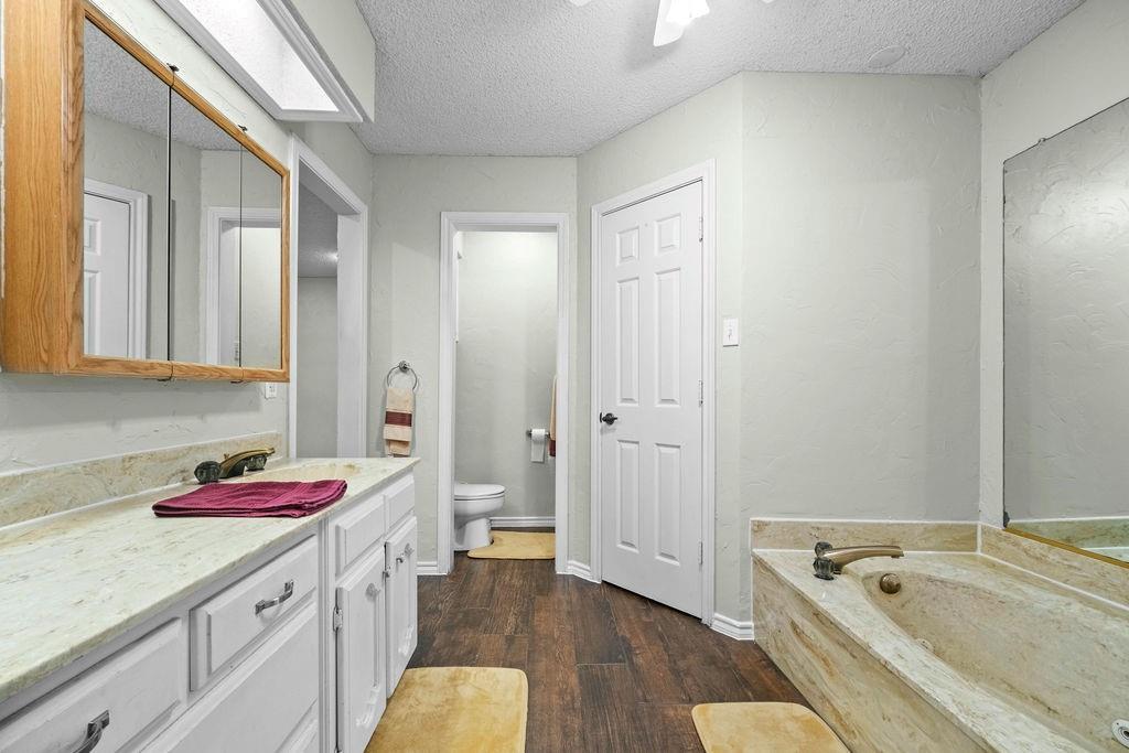 6939 Calender Road Arlington, TX 76001 - Photo 13 of 40 Bathroom featuring vanity, a garden tub, toilet, wood finished floors, and a textured ceiling