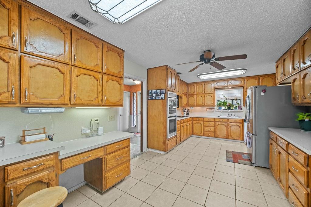 6939 Calender Road Arlington, TX 76001 - Photo 14 of 40 Kitchen with a ceiling fan, brown cabinetry, light countertops, a textured ceiling, and light tile patterned floors