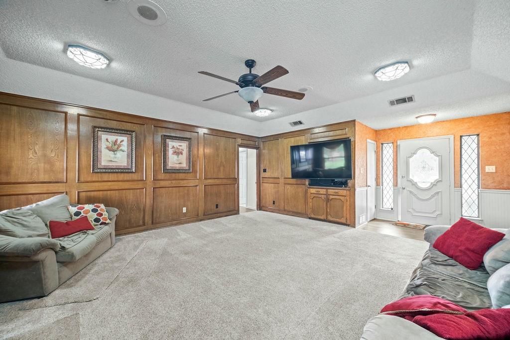 6939 Calender Road Arlington, TX 76001 - Photo 15 of 40 Living area with a textured ceiling, a ceiling fan, a decorative wall, and light colored carpet