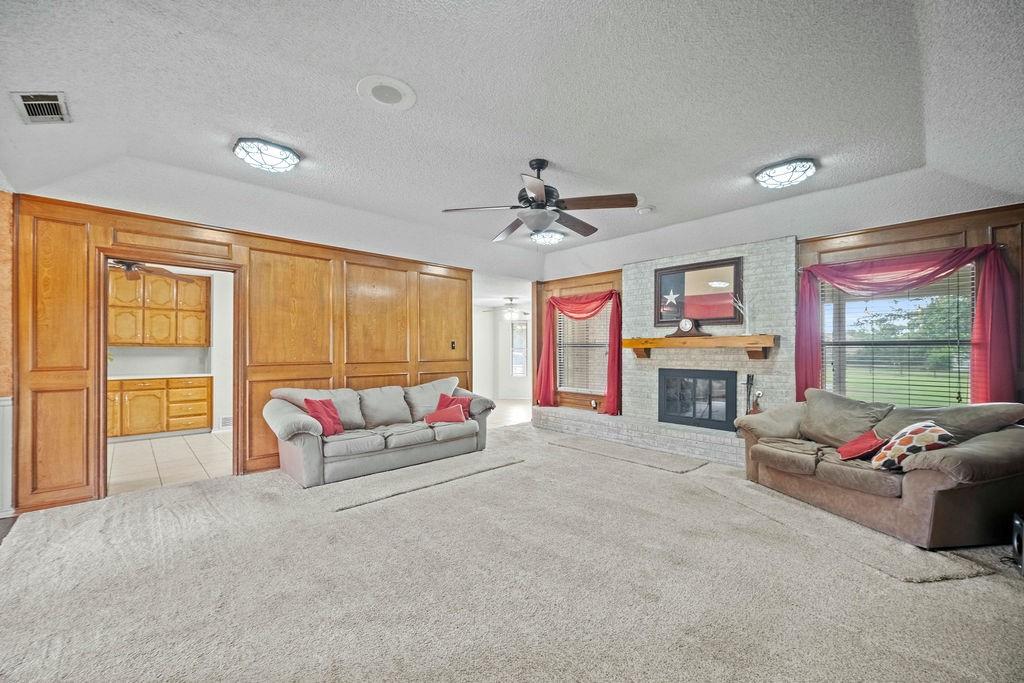 6939 Calender Road Arlington, TX 76001 - Photo 18 of 40 Living area with a textured ceiling, light carpet, a ceiling fan, a brick fireplace, and lofted ceiling