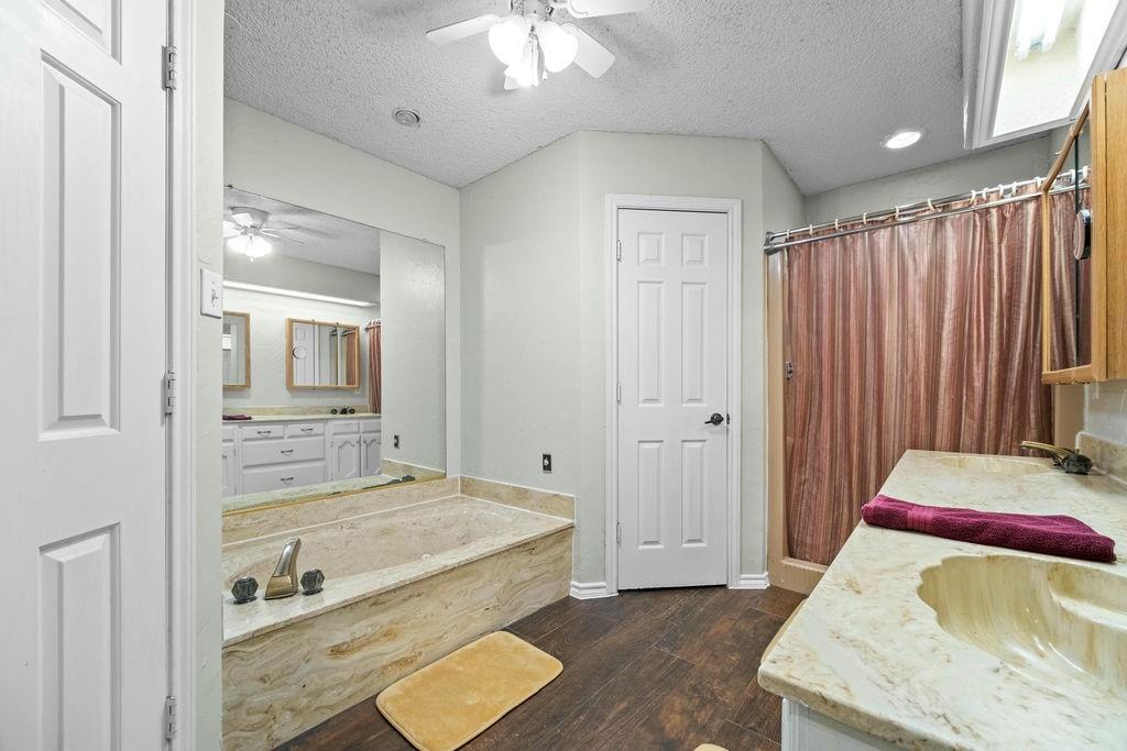 6939 Calender Road Arlington, TX 76001 - Photo 22 of 40 Bathroom with a ceiling fan, vanity, hardwood / wood-style flooring, a garden tub, and a textured ceiling