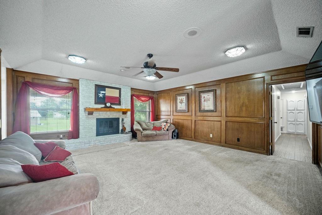 6939 Calender Road Arlington, TX 76001 - Photo 25 of 40 Carpeted living room with a textured ceiling, ceiling fan, a brick fireplace, lofted ceiling, and wooden walls