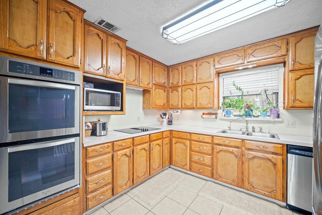 6939 Calender Road Arlington, TX 76001 - Photo 26 of 40 Kitchen with appliances with stainless steel finishes, a sink, light countertops, a textured ceiling, and brown cabinets