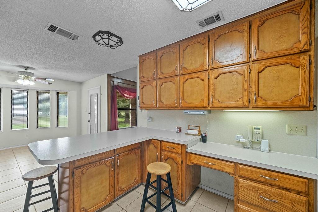 6939 Calender Road Arlington, TX 76001 - Photo 33 of 40 Kitchen with a peninsula, brown cabinets, light countertops, a textured ceiling, and light tile patterned floors