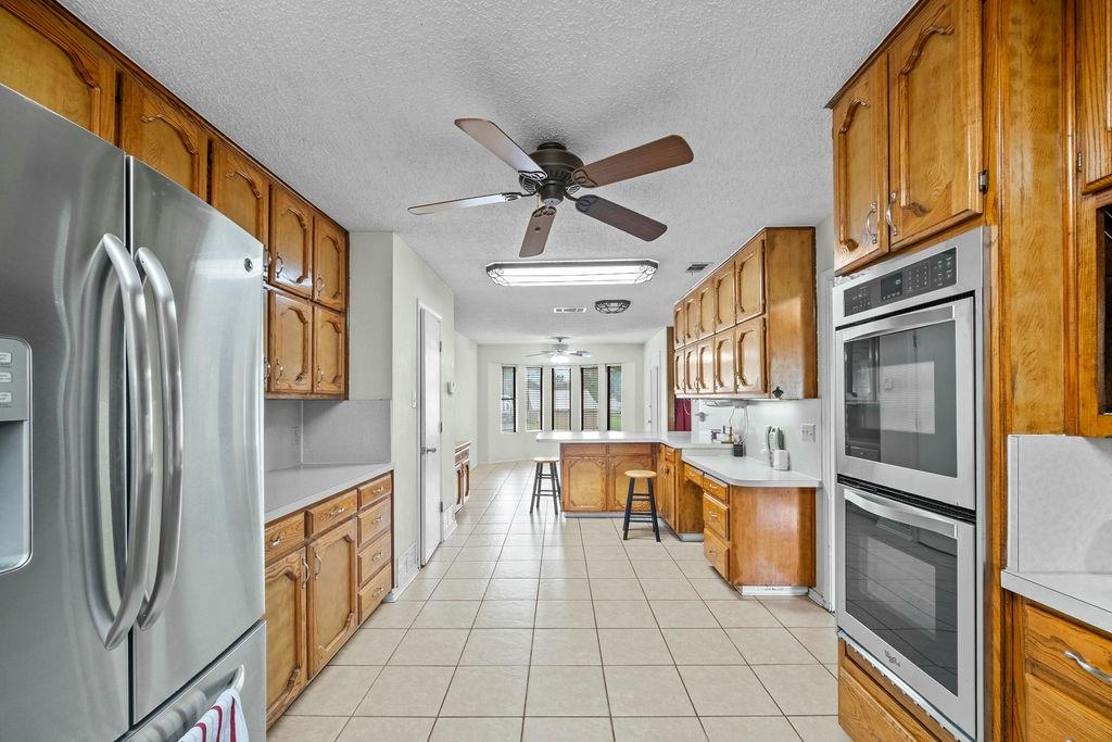 6939 Calender Road Arlington, TX 76001 - Photo 35 of 40 Kitchen featuring appliances with stainless steel finishes, a ceiling fan, a textured ceiling, brown cabinetry, and light tile patterned flooring