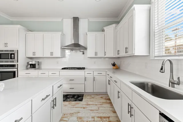 a large white kitchen with stainless steel appliances granite countertop a sink dishwasher stove and white cabinets with wooden floor