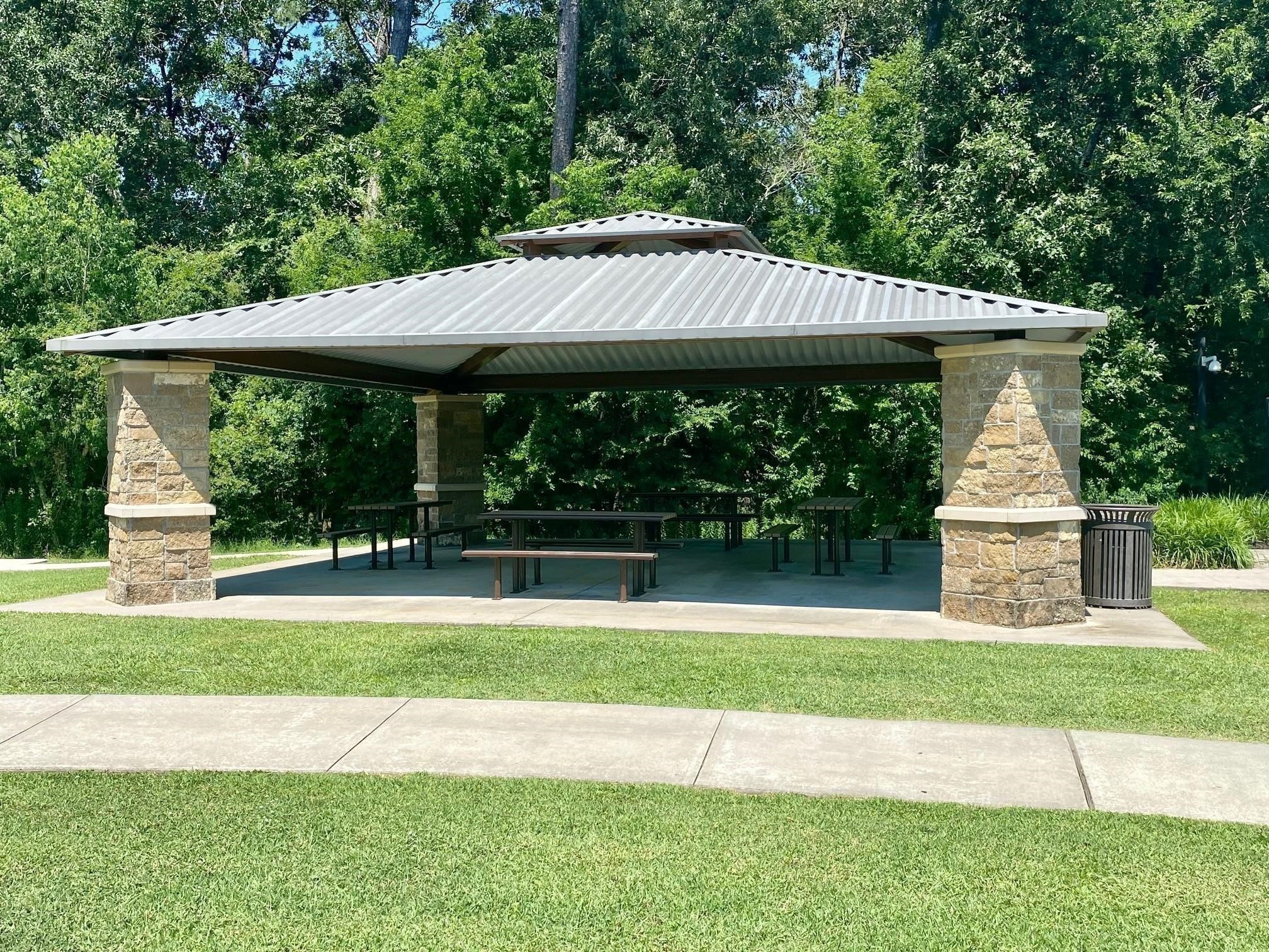 438 Vane Way Crosby, TX 77532 - Photo 13 of 21 This photo shows a covered picnic pavilion with stone pillars and a metal roof set in a lush, green park area, ideal for outdoor gatherings and relaxation.
