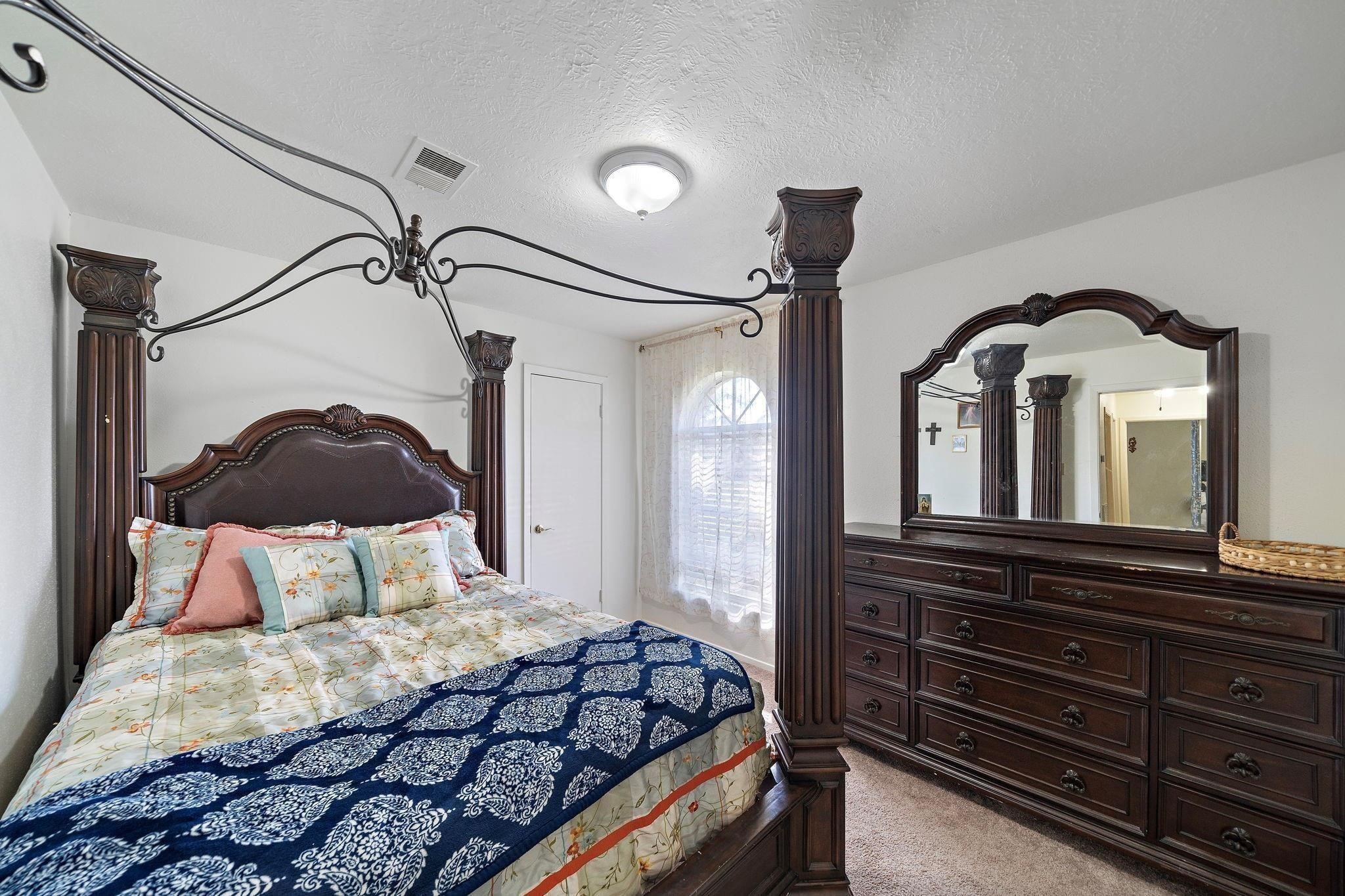 438 Vane Way Crosby, TX 77532 - Photo 5 of 21 This bedroom features a classic, elegant design with a large four-poster bed and matching dark wood furniture, including a dresser with a large mirror. The room is well-lit with a window covered by sheer curtains, creating a cozy and inviting atmosphere.