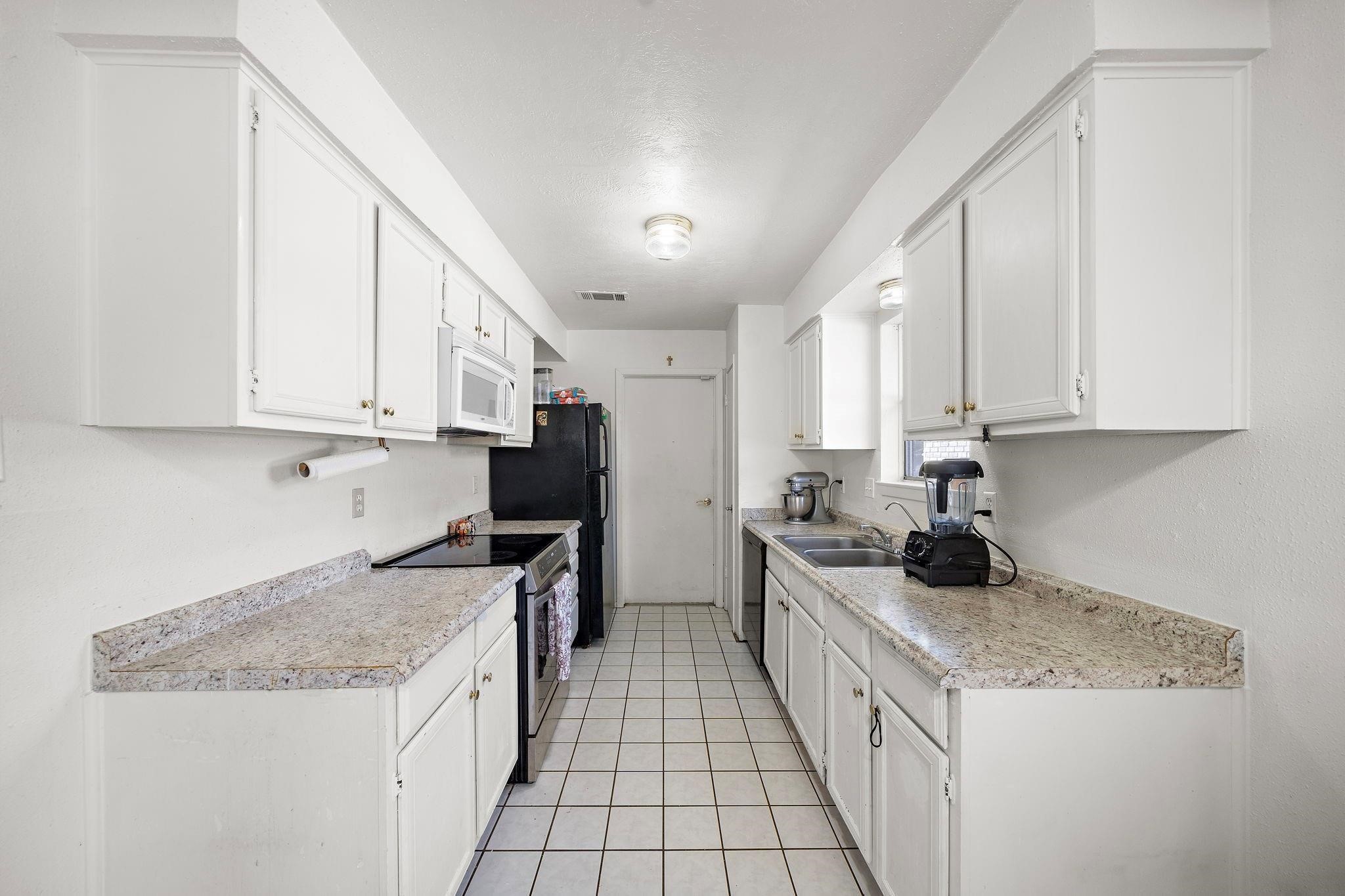 438 Vane Way Crosby, TX 77532 - Photo 9 of 21 This kitchen features a galley layout with white cabinetry, granite-style countertops, and modern appliances. It has ample storage and counter space, with a clean, bright design ideal for efficient meal preparation.