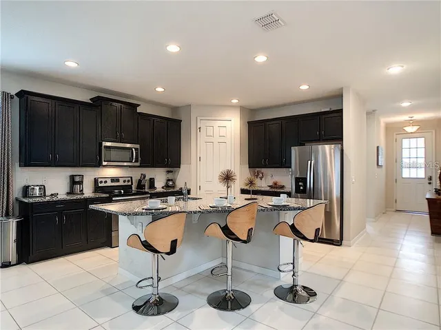 a kitchen with stainless steel appliances granite countertop a refrigerator a stove a sink dishwasher a dining table and chairs with wooden cabinets