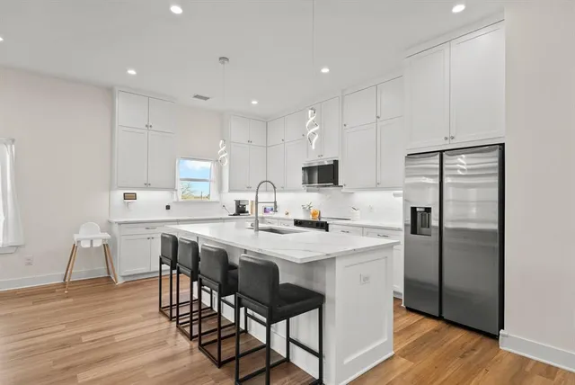 a kitchen with stainless steel appliances a sink a stove a refrigerator with white cabinets and wooden floor