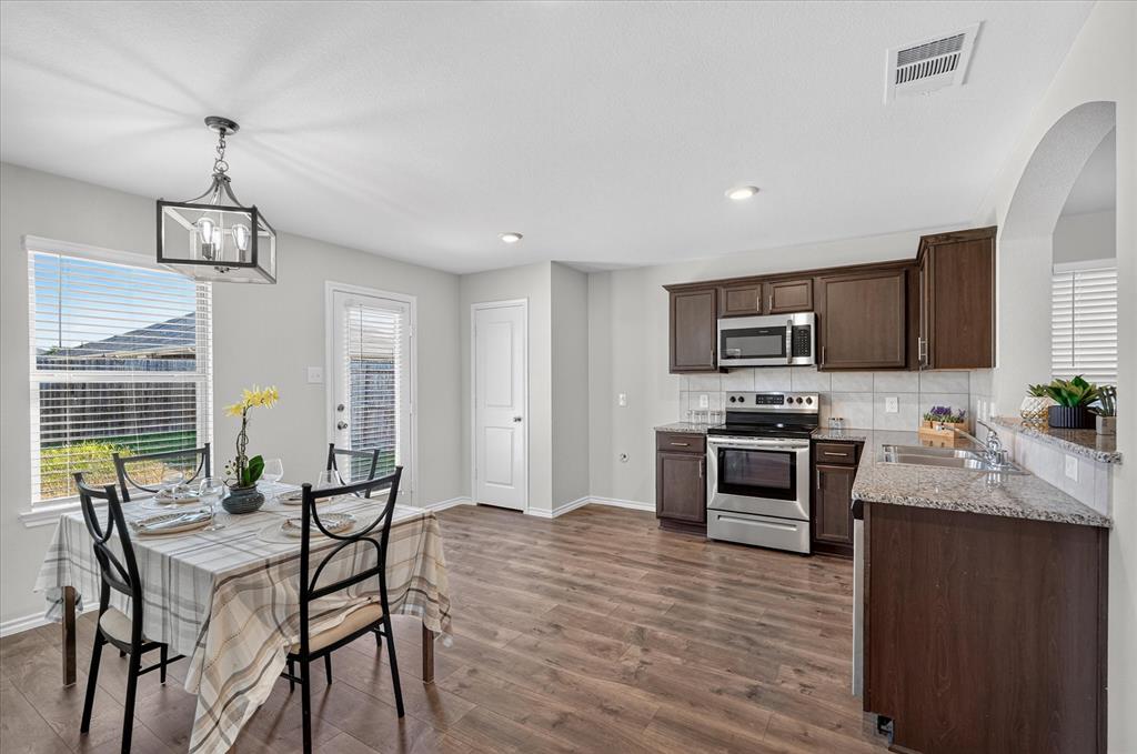 2428 Rosharon Drive Forney, TX 75126 - Photo 7 of 40 Spacious kitchen and dining area featuring wood-finish flooring, stainless steel appliances, dark wood cabinetry, and light-toned countertops