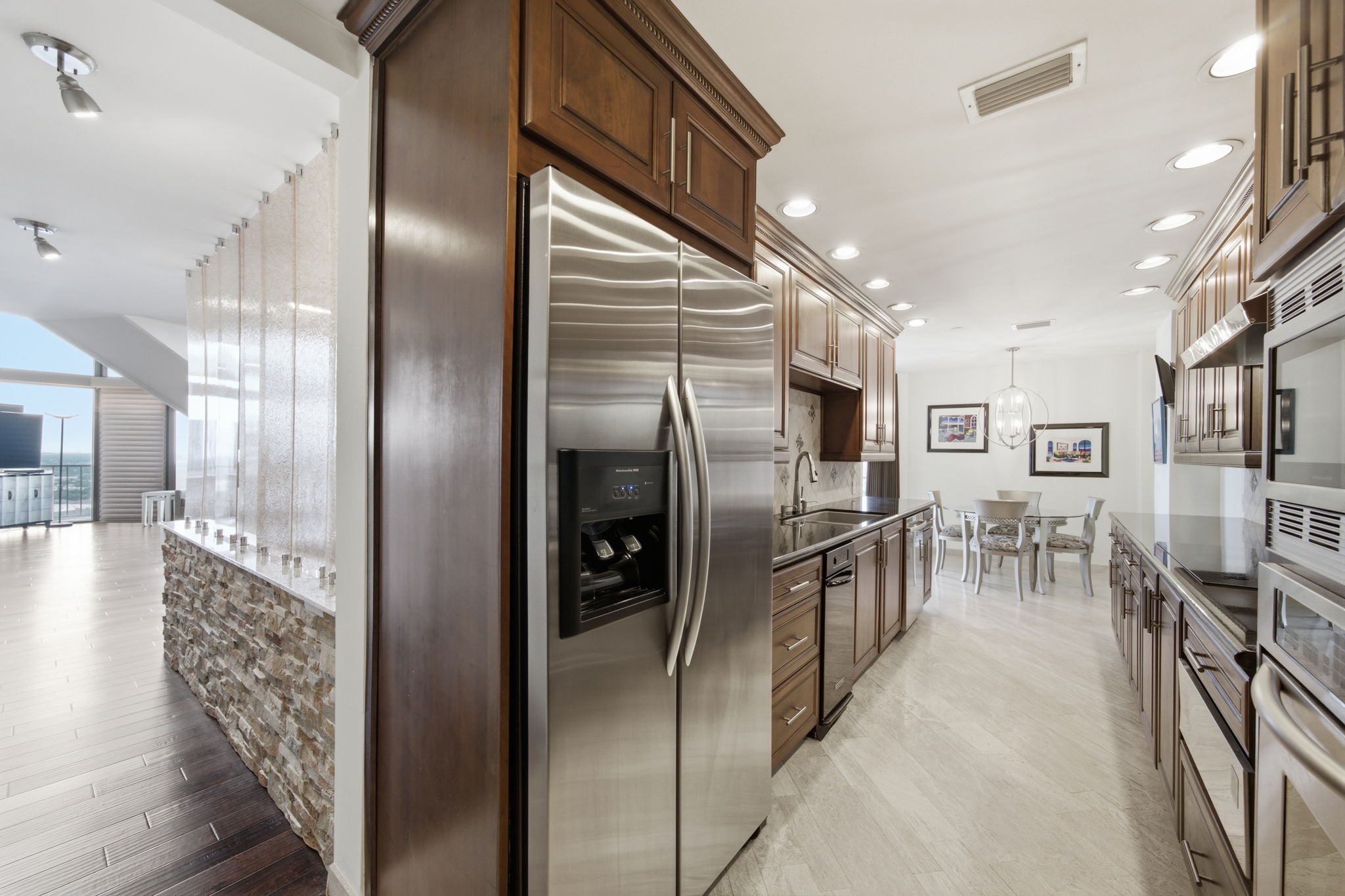 3350 McCue Road, Unit 2402 Houston, TX 77056 - Photo 21 of 49 Gleaming stainless steel appliances, including built-in double ovens and an expansive French door refrigerator, elevate this sophisticated galley kitchen. Luxurious granite countertops and warm wood cabinetry flow effortlessly toward a bright casual dining area framed by modern lighting.