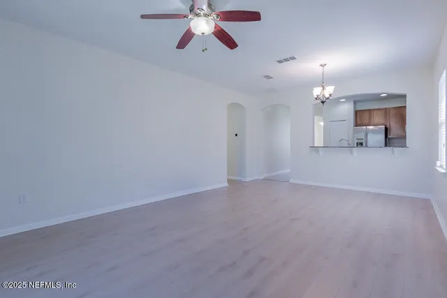 an empty room with chandelier fan and windows