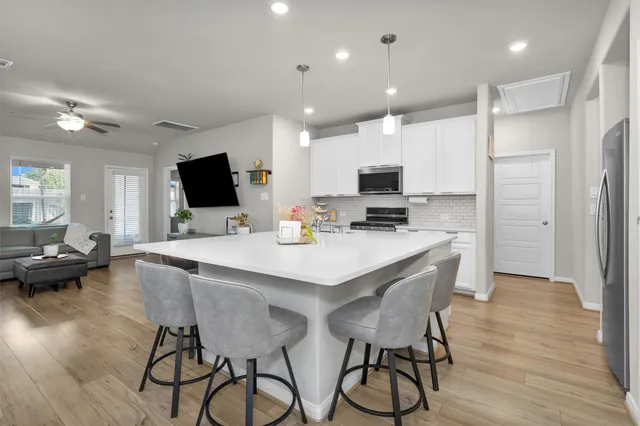 a kitchen with stainless steel appliances kitchen island granite countertop a stove a refrigerator a sink a dining table and chairs with wooden floor