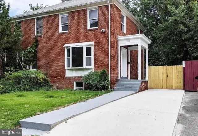 a view of a brick house with a yard plants and large tree
