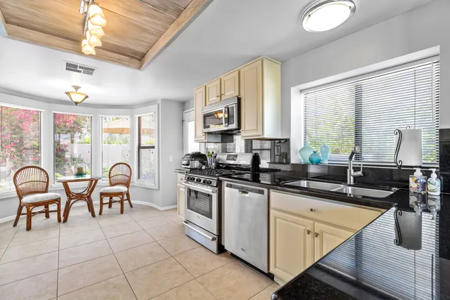 a kitchen with stainless steel appliances granite countertop a stove top oven a sink a counter space and living room view