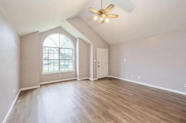 an empty room with wooden floor fan and windows