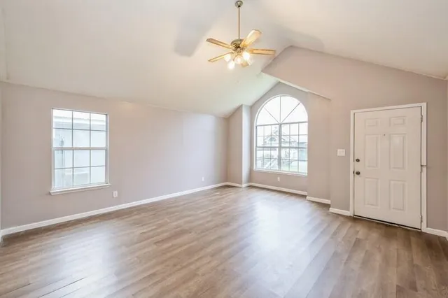 an empty room with wooden floor chandelier fan and windows
