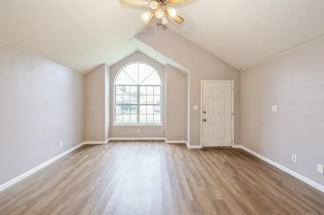 an empty room with wooden floor chandelier fan and windows