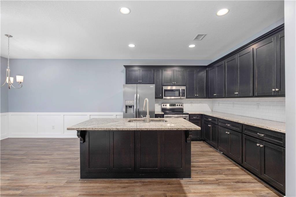 70 Apache Trail Fort Mitchell, AL 36856 - Photo 21 of 33 Kitchen with light stone countertops, stainless steel appliances, a center island with sink, light wood-type flooring, and wainscoting