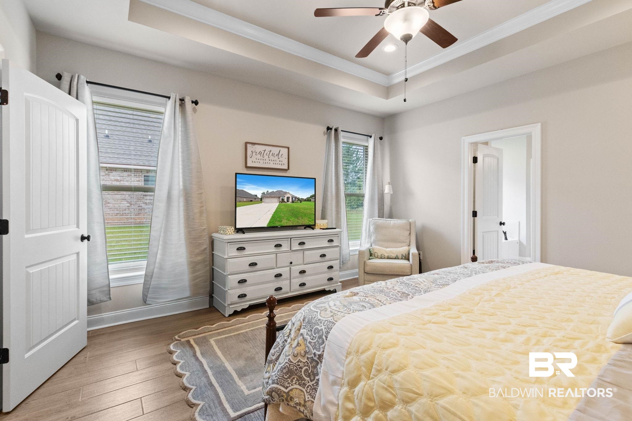 22244 Hibiscus Circle Foley, AL 36535 - Photo 38 of 51 Spacious bedroom featuring wood-finish flooring, a tray ceiling with a ceiling fan, and two windows with blinds