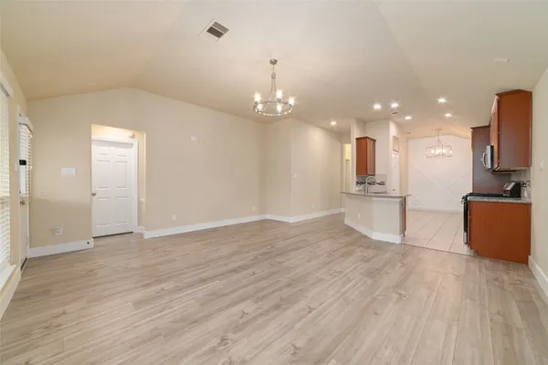 a view of empty room with wooden floor and kitchen view