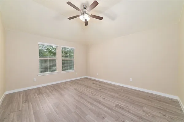 an empty room with wooden floor fan and windows