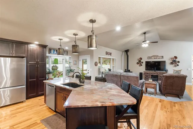 a kitchen with stainless steel appliances kitchen island granite countertop a refrigerator a stove a sink a dining table and chairs with wooden floor