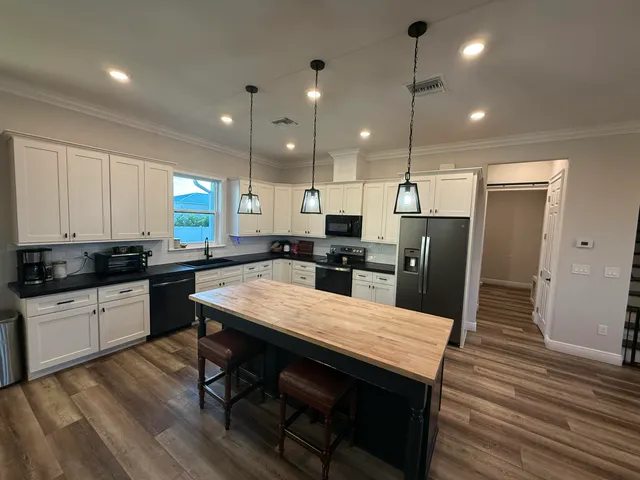 a kitchen with stainless steel appliances granite countertop a refrigerator a sink dishwasher a stove and white cabinets with wooden floor