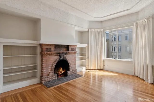 a view of an empty room with wooden floor fireplace and a window