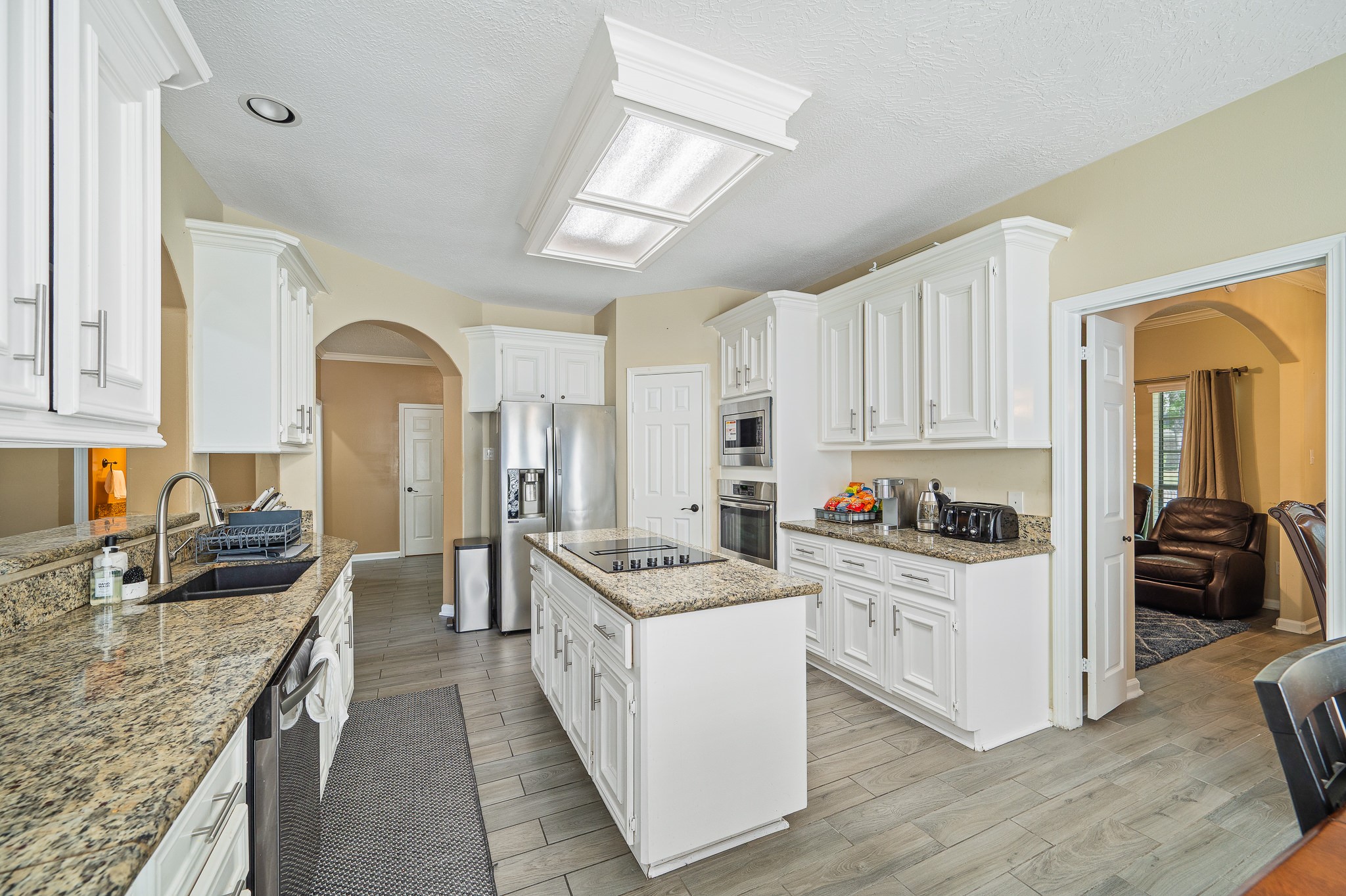 8111 Morningbrook Court Spring, TX 77379 - Photo 14 of 46 a kitchen with stainless steel appliances granite countertop a stove top oven a sink a refrigerator white cabinets and couches with wooden floor