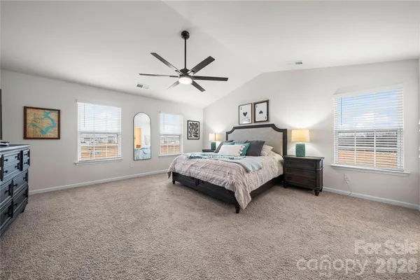 a spacious bedroom with a large bed a chandelier and windows