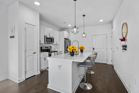a kitchen with stainless steel appliances granite countertop a sink dishwasher a refrigerator a microwave oven a stove and a dining table with wooden floor