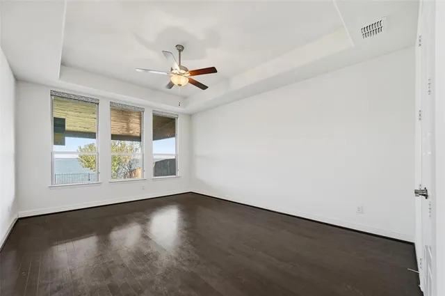 an empty room with wooden floor chandelier fan and windows