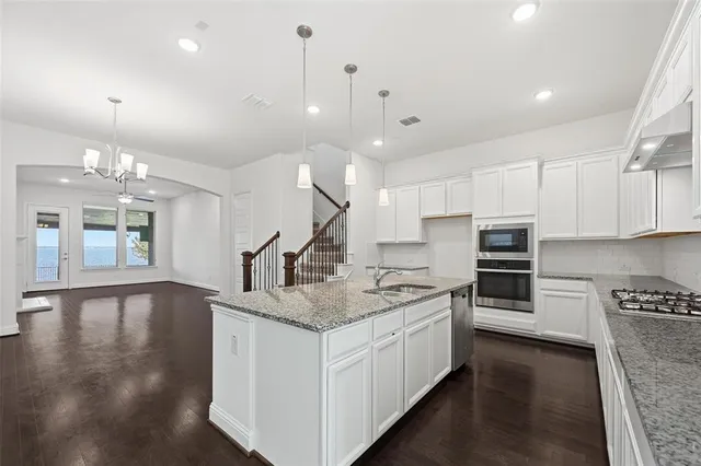 a kitchen with stainless steel appliances granite countertop a sink a stove and a wooden floors