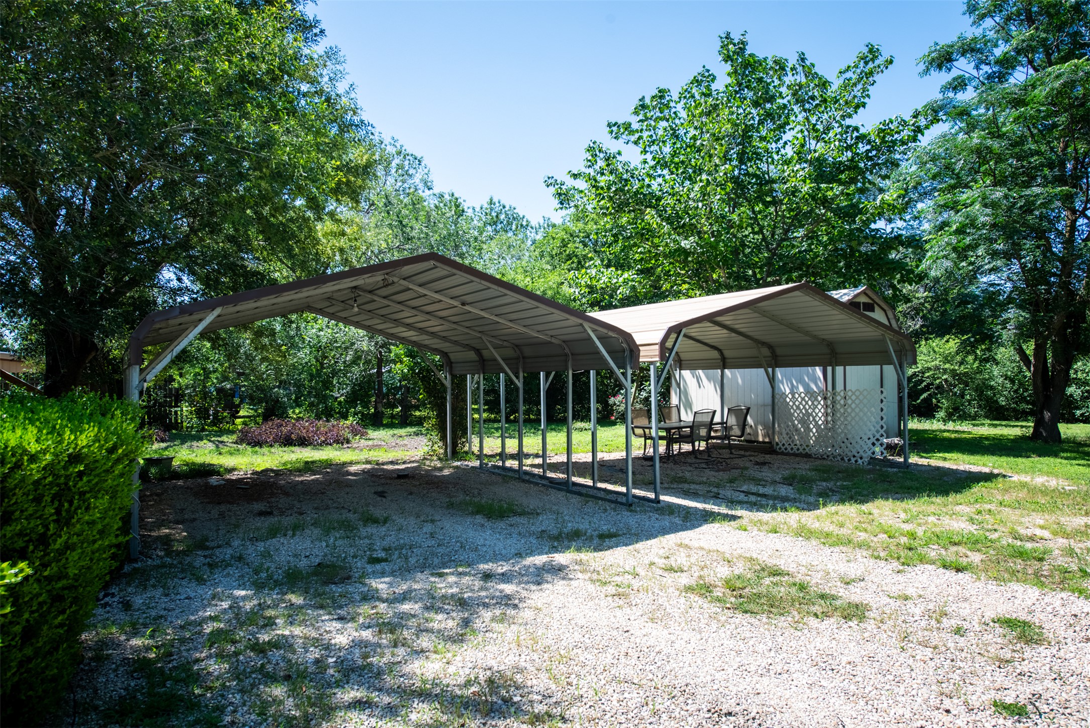 258 Quail Ridge Drive Kyle, TX 78640 - Photo 7 of 11 Gravel driveway leading to two attached metal carports, offering covered parking and an additional covered outdoor area with privacy lattice