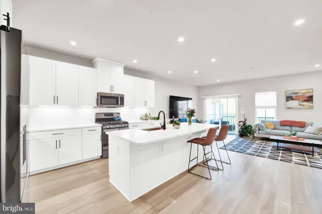 a kitchen with stainless steel appliances a stove a sink a refrigerator white cabinets and couches with wooden floor