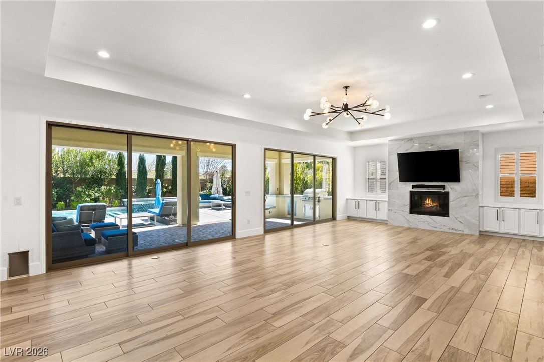 4039 Villa Rafael Drive Las Vegas, NV 89141 - Photo 14 of 45 Unfurnished living room featuring a raised ceiling, a chandelier, light wood-type flooring, a premium fireplace, and recessed lighting