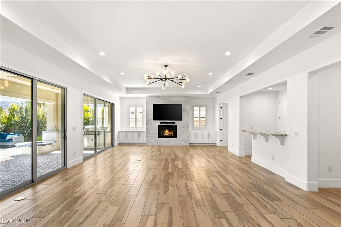 4039 Villa Rafael Drive Las Vegas, NV 89141 - Photo 17 of 45 Unfurnished living room featuring a chandelier, wood tiled floors, a tray ceiling, a fireplace, and recessed lighting