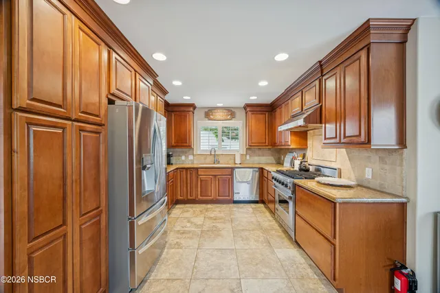 a large kitchen with stainless steel appliances granite countertop a refrigerator a sink dishwasher and wooden cabinets with wooden floor