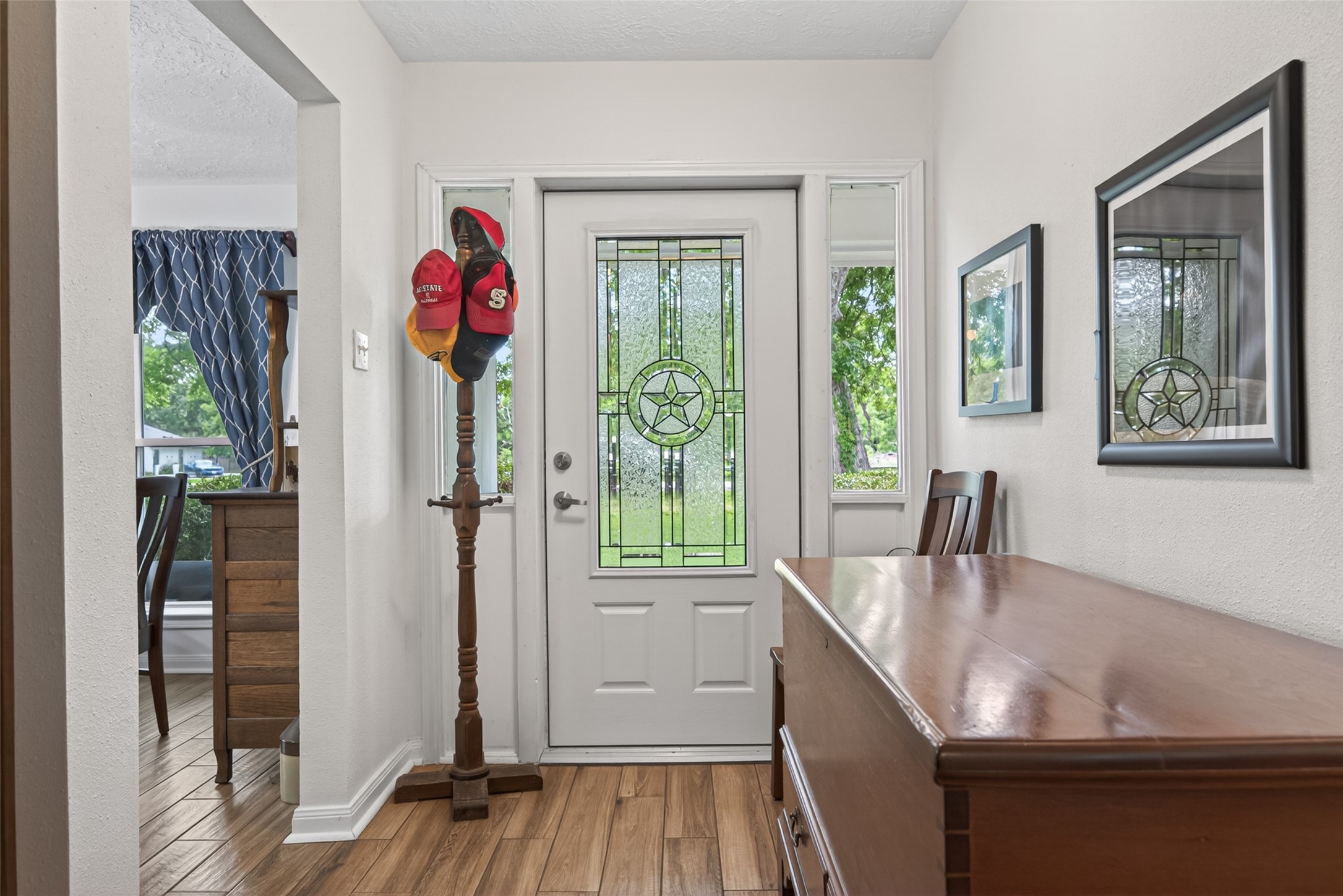 1004 Wagon Road Simonton, TX 77485 - Photo 4 of 40 Step inside to a bright and welcoming entryway featuring warm wood-look flooring and crisp white walls. The charming front door with its decorative leaded glass star panel and flanking sidelights allows natural light to filter in beautifully. This inviting space opens seamlessly into the heart of the home.