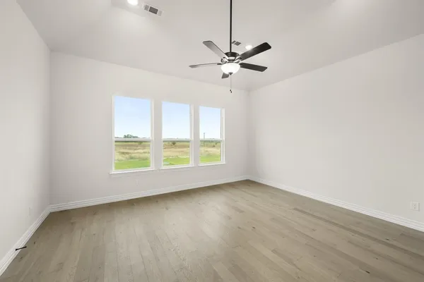 an empty room with wooden floor fan and windows