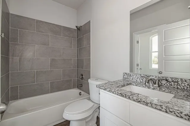 a bathroom with a granite countertop bathtub sink vanity mirror and toilet