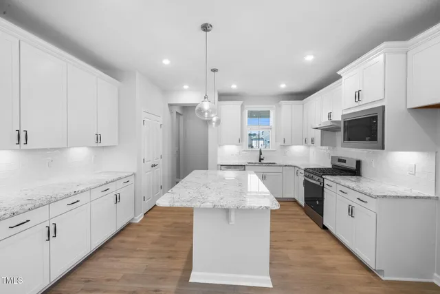 a large kitchen with stainless steel appliances kitchen island granite countertop a stove top oven a sink dishwasher and a refrigerator with white cabinets