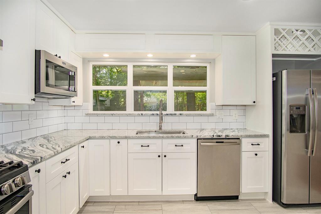 a kitchen with granite countertop a sink cabinets stainless steel appliances and a window