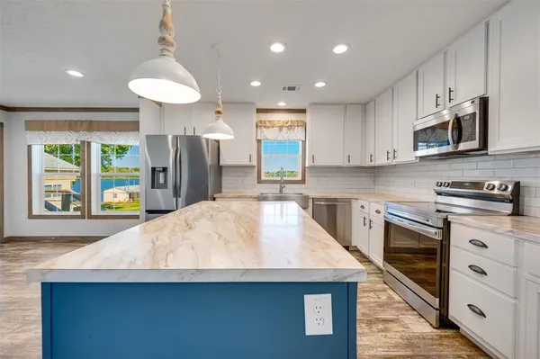 a kitchen with stainless steel appliances granite countertop a kitchen island a stove a sink a microwave a refrigerator and cabinets