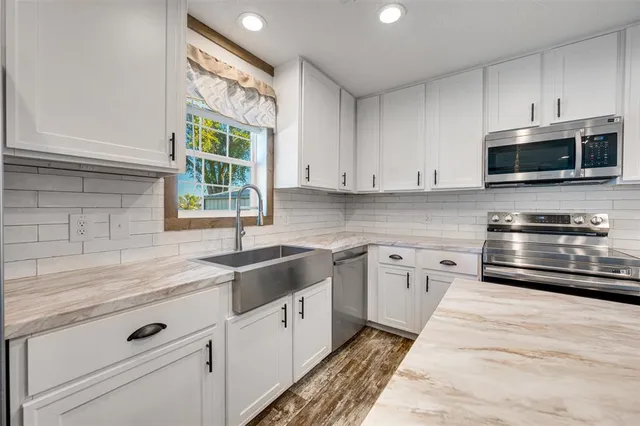 a kitchen with granite countertop white cabinets stainless steel appliances and a window